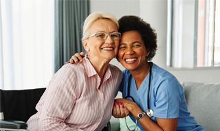 A smiling elderly woman in a wheelchair and a cheerful nurse embrace each other. photo